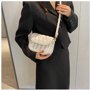 Detail of cream white pleated crossbody bag with gold hardware on black blazer suit