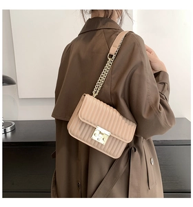 Detail der beige plissierten Umhängetasche mit goldenem Verschluss und Kettengurt an Model