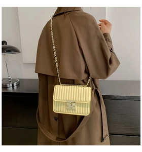 Detail der blassgelben gesteppten Umhängetasche mit goldener Kette auf einem Modell