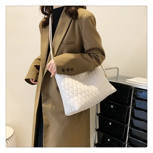 Side view of a white quilted tote bag with diamond pattern and slim leather straps