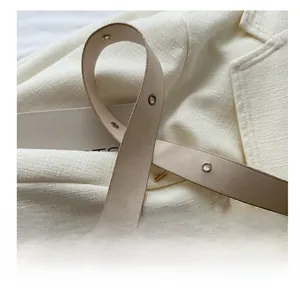 Detail of beige leather shoulder strap with silver eyelets and fine stitching on a bag