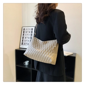 Detail of beige quilted bucket bag with gold hardware worn by a model in a black suit