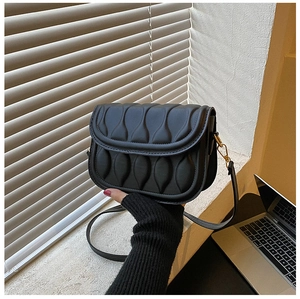 Detail of black quilted saddle bag featuring wave texture and adjustable shoulder strap