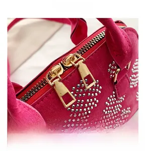 Détail macro de la double fermeture éclair dorée et strass brillants sur le sac en daim fuchsia