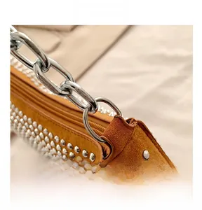 Macro detail of silver chain strap and metal rivet hardware on a brown suede shoulder bag