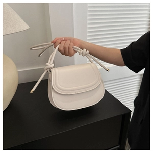 Detail view of cream saddle bag featuring unique knot strap and gold metal hardware