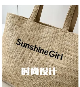 Detail of woven straw tote bag featuring SunshineGirl embroidery and faux leather handles