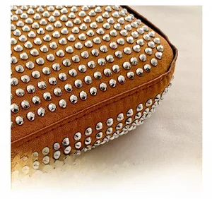 Close-up of brown suede bag featuring silver metal studs and precision stitching detail
