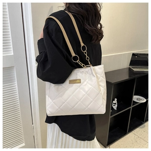 Close-up of white quilted tote bag featuring gold chain strap and fashion label on front