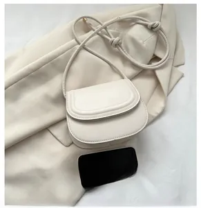 Detailed top view of a cream leather crossbody bag next to a smartphone for size comparison