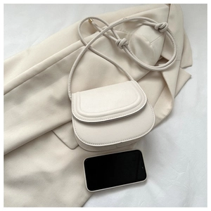 Detail of minimalist cream saddle bag showing fine stitching and size reference next to phone
