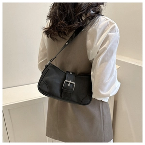Close-up of black leather shoulder bag with silver buckle worn by a model in a minimal setting