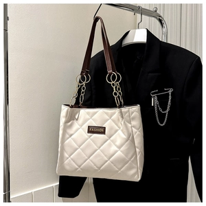 Detail of cream quilted tote bag with brown leather handles and gold chain accents