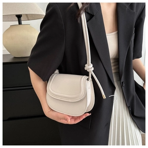 Detail of a creamy white semi-circle crossbody bag with unique knot shoulder strap detail