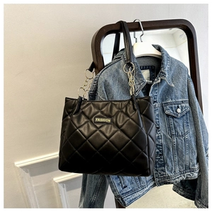 Detail of black quilted tote bag with gold chain strap and fashion label on denim