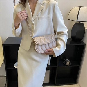 Beige quilted shoulder bag with wavy texture and golden hardware shown on a model