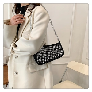 Close-up of black rivet shoulder bag with silver chain strap worn on cream blazer