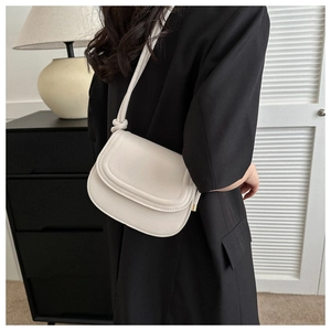 Detail of a minimalist cream saddle bag with unique knotted strap on a modern background