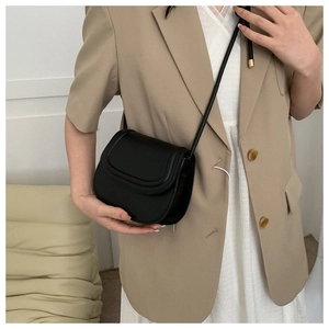 Minimalist black matte saddle bag with curved flap and gold hardware on female model
