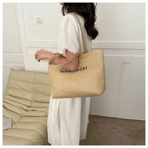 Detail of woven straw tote bag with black Sunshine Girl text and faux leather straps