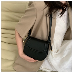 Detail of black leather crossbody bag featuring knot strap and gold metal accents