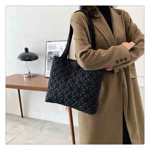 Detail of black quilted tote bag with geometric stitching on wool coat model
