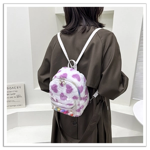 Détail d'un mini sac à dos en peluche à cœurs violets et poche avec pompons colorés
