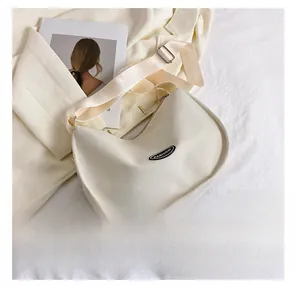 Detail of cream hobo bag with wide shoulder strap beside a phone for size reference