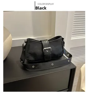 Detail of a black semi-circular crossbody bag with wide buckle and eyelet strap details