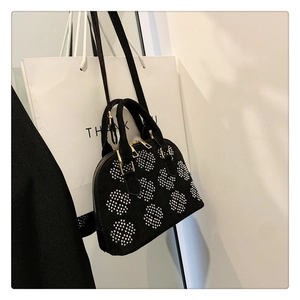 Détail du sac coquille en daim noir avec clous argentés, zip doré et bandoulière