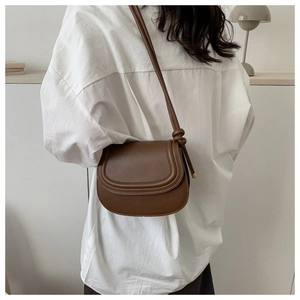 Brown saddle bag with double stitching detail worn by model in minimalist casual setting