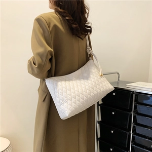 Minimalist white quilted bucket bag with knot shoulder strap worn by a model in casual style
