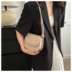 Chic beige saddle bag with knot strap detail worn over a black blazer and white skirt