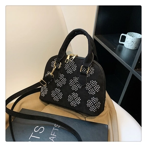 Détail du sac coquillage en daim noir avec motif clouté et accessoires métalliques