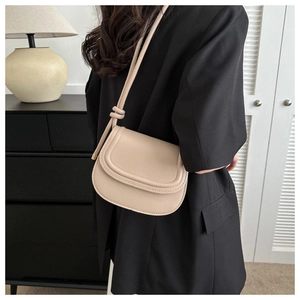 Detail view of cream saddle bag featuring a unique knotted shoulder strap and matte leather texture