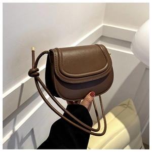 Detail of a brown leather saddle bag featuring a flap closure and knotted strap decor
