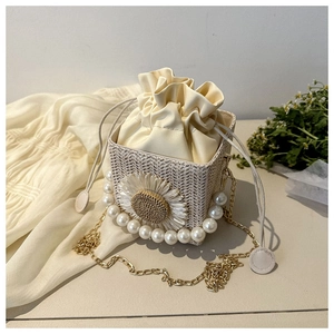 Close-up of woven straw bag with white daisy flower, pearl handle and gold chain detail