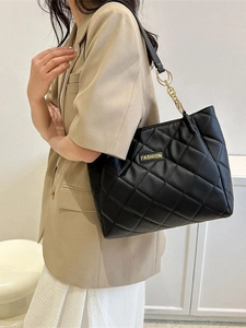 Chic black quilted tote bag with golden chain strap and fashion plate on shoulder