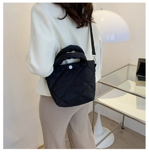 Detail of black quilted puffer handbag with soft handle and white button detail