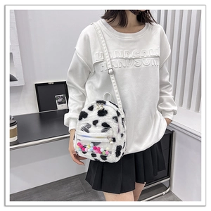 Détail du sac à dos en peluche à motif vache avec poche cœur et pompons colorés