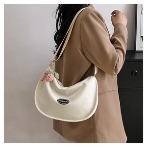 Detail of off-white crescent canvas bag with a cute knit strawberry pendant and fashion tag
