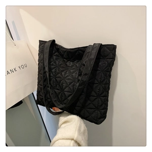 Detail of black quilted large tote bag with geometric pattern and long shoulder strap