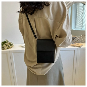 Petit sac bandoulière minimaliste en cuir PU noir porté par un mannequin dans un intérieur