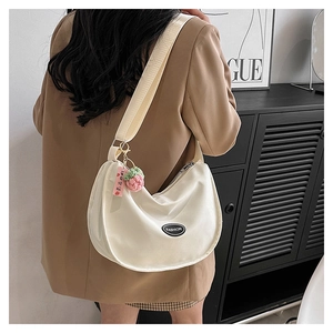 Close-up of white nylon crescent bag with adjustable strap and pink strawberry charm