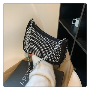 Close-up of black rivet studded baguette bag with silver chain strap held by a person
