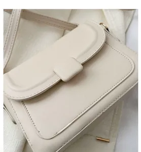 Detail of cream-white flap crossbody bag featuring gold hardware and fine stitching