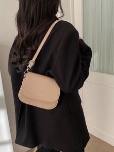 Minimalist beige crossbody bag with gold text on flap, shown on a black suit jacket