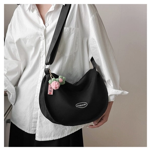 Detail of a black crescent crossbody bag with a fashion tag and floral crochet charm