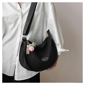 Detail of black crescent crossbody bag with plush strawberry charm and wide strap