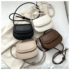 Flat lay of women's saddle bags in black, white, mocha, and beige with knot straps